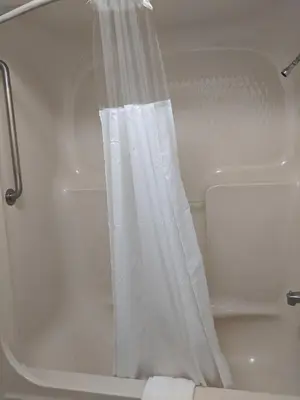 a white shower curtain in a bathtub with at Falls Lodge & Suites in Niagara Falls