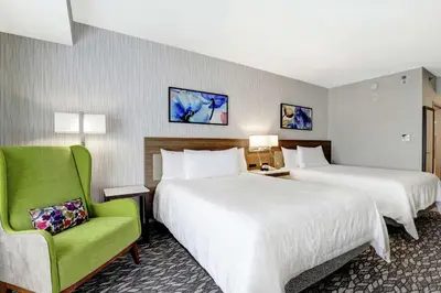 a hotel room with two beds and a green chair at Hilton Garden Inn Toronto/Ajax in Ajax