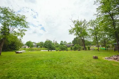 a large grassy field with trees in the background at Beautiful 3 Bdrm + Bunkie Waterfront Cottage Near Gull Lake in Minden