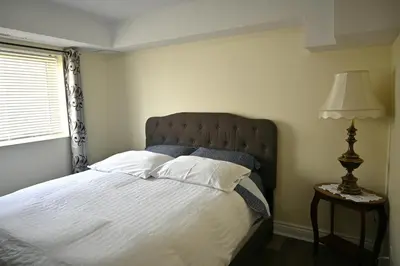 a bedroom with a bed and a lamp and a window at Empire Suite in Niagara Falls