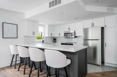 a kitchen with white cabinets and a bar with white stools at Ski in Ski Out Condo at Blue Mountain Close to Village in Blue Mountains