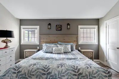 a bedroom with a large bed and two windows at Sandy Cove Cottage in Crystal Beach