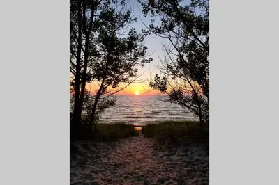a sunset over the water with trees on a beach at Cottage with River Front & minutes away from Beach in Wasaga Beach
