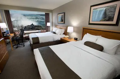 a hotel room with two beds and a desk at The Oakes Hotel Overlooking the Falls in Niagara Falls
