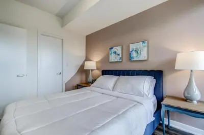 a bedroom with a large white bed and two lamps at The Benetton Suite - Square One 1 BR + Den + 1 Parking in Mississauga