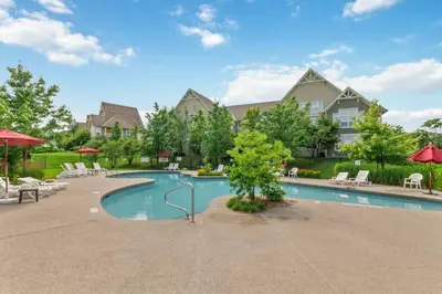 a pool with chairs and umbrellas in front of a house at Rivergrass Townhouse in Blue with Pool Golf Skiing - 219 Rivergrass in Blue Mountains