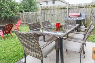 a glass table with chairs and a grill in a backyard at Family-Friendly Boho Stay - Sleeps 10 - Near the Falls in Thorold