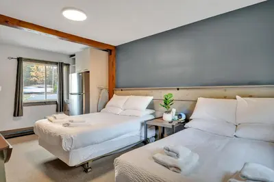 a bedroom with two beds and a table and a window at Moira Lake Motel in Madoc