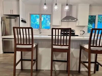 a kitchen with three wooden bar stools in front of a counter at Marmora Hideaway - Lake front in Marmora