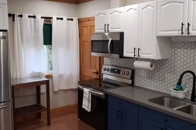 a kitchen with white cabinets and a black stove top oven at Modern Chic Cottage - Hot Tub, Sauna, Tay Trail in Waubaushene