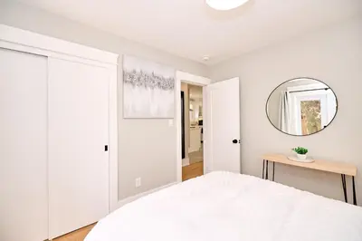a white bedroom with a bed and a mirror at The Newark House in Niagara on the Lake